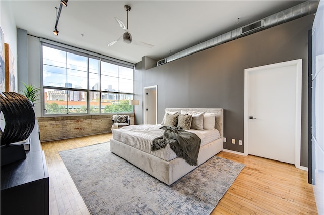 bedroom with ceiling fan, light hardwood / wood-style flooring, and brick wall