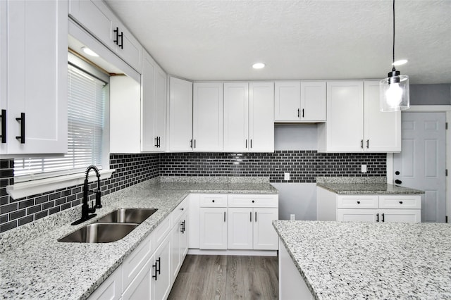 kitchen with decorative light fixtures, white cabinetry, light hardwood / wood-style floors, and sink