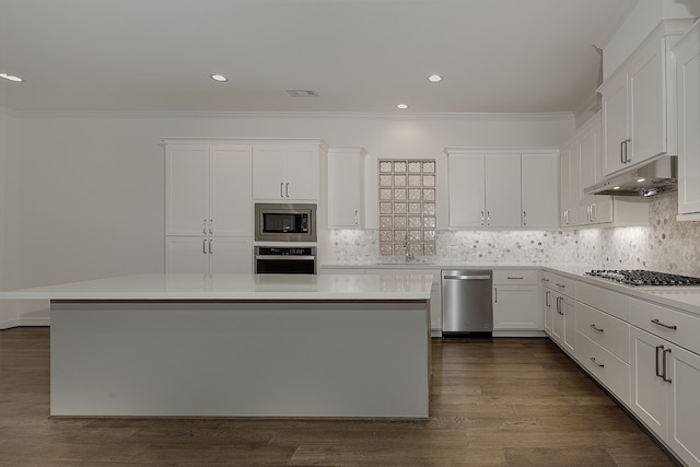 kitchen with appliances with stainless steel finishes, backsplash, white cabinets, dark hardwood / wood-style floors, and a kitchen island