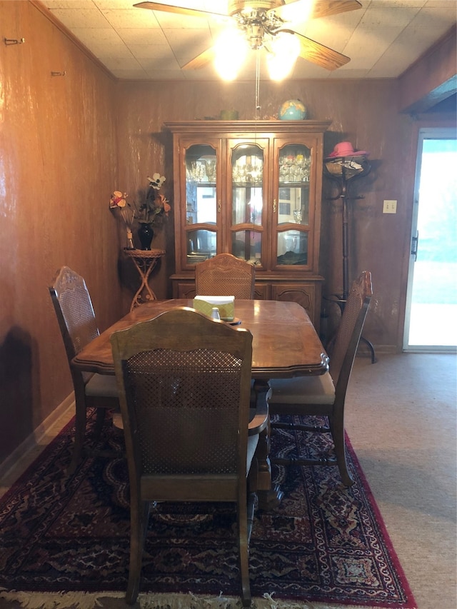 carpeted dining area featuring ceiling fan and wood walls