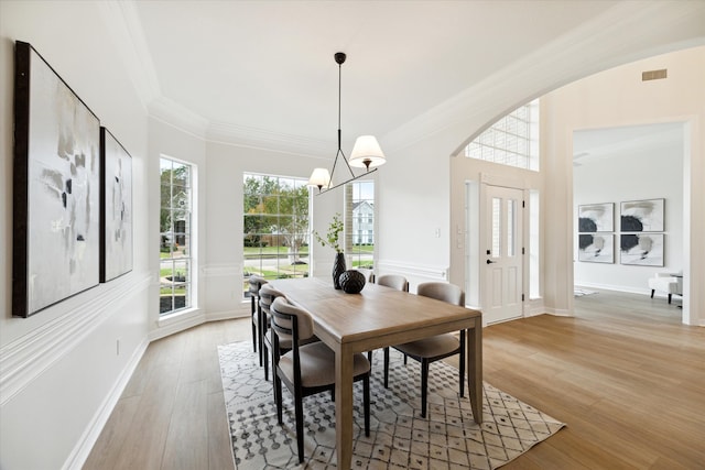 dining space featuring light hardwood / wood-style floors, crown molding, and an inviting chandelier