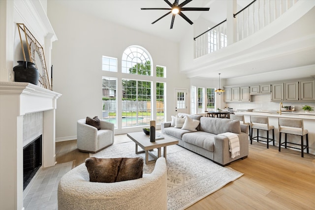 living room featuring light wood-type flooring, ceiling fan, sink, a high ceiling, and a tiled fireplace