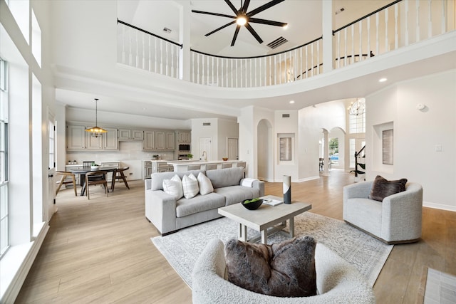 living room with ceiling fan with notable chandelier, light wood-type flooring, and a high ceiling