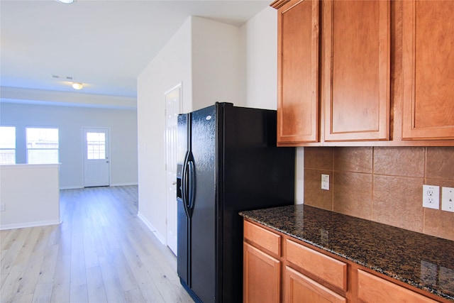 kitchen with baseboards, decorative backsplash, light wood-style flooring, dark stone countertops, and black refrigerator with ice dispenser