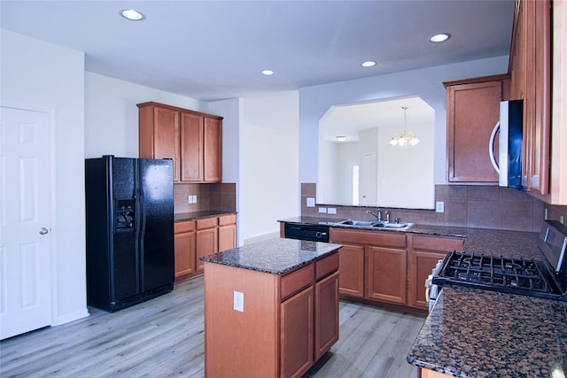 kitchen with brown cabinetry, a sink, a kitchen island, light wood-type flooring, and black appliances