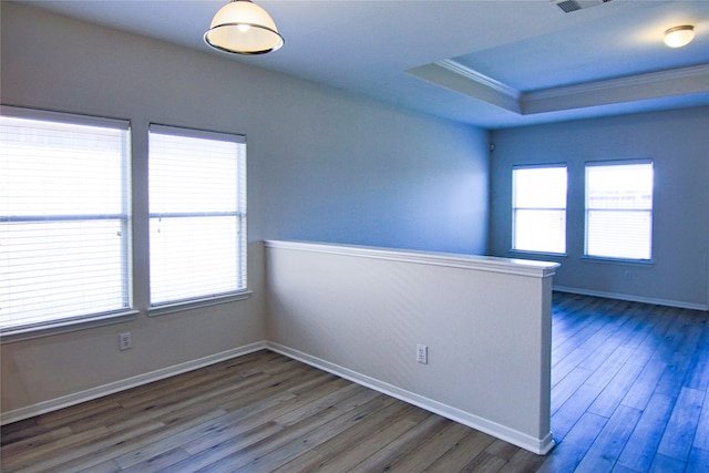 empty room with crown molding, baseboards, a raised ceiling, and wood finished floors