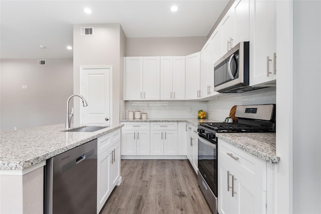 1319 E 35th St, Houston, TX 77022 - kitchen featuring stainless steel appliances, a sink, light wood finished floors, backsplash, and white cabinetry