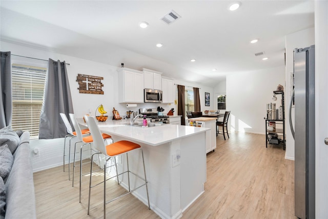 kitchen with kitchen peninsula, white cabinetry, light hardwood / wood-style flooring, and appliances with stainless steel finishes