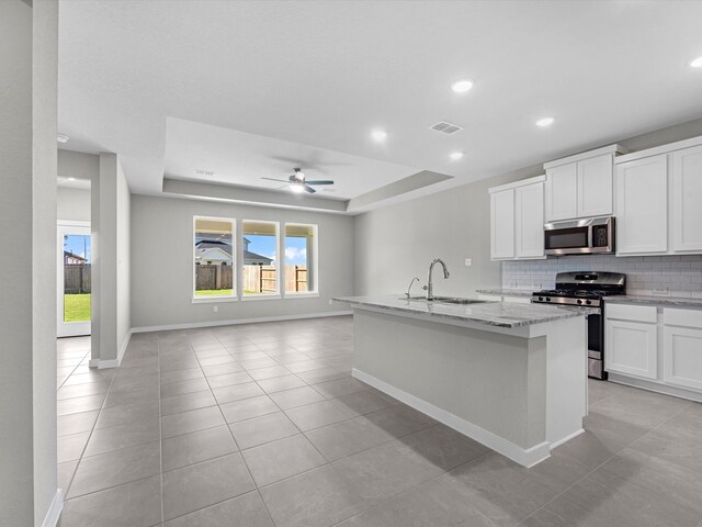 kitchen with light stone countertops, stainless steel appliances, sink, white cabinets, and an island with sink