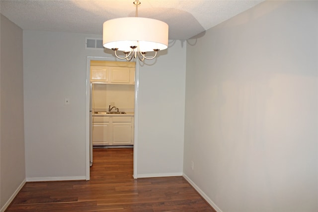 unfurnished dining area featuring a textured ceiling, a notable chandelier, sink, and dark wood-type flooring