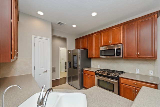 kitchen with decorative backsplash, sink, stainless steel appliances, and a textured ceiling