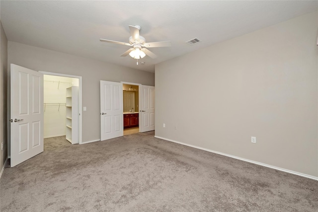 unfurnished bedroom with carpet floors, a closet, a spacious closet, and ceiling fan