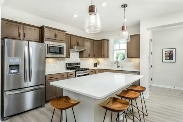 kitchen featuring sink, a center island, pendant lighting, a breakfast bar, and appliances with stainless steel finishes