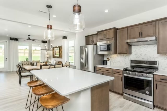 kitchen featuring ceiling fan, a center island, stainless steel appliances, and decorative light fixtures