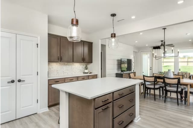 kitchen with ceiling fan, hanging light fixtures, dark brown cabinets, a kitchen island, and light wood-type flooring