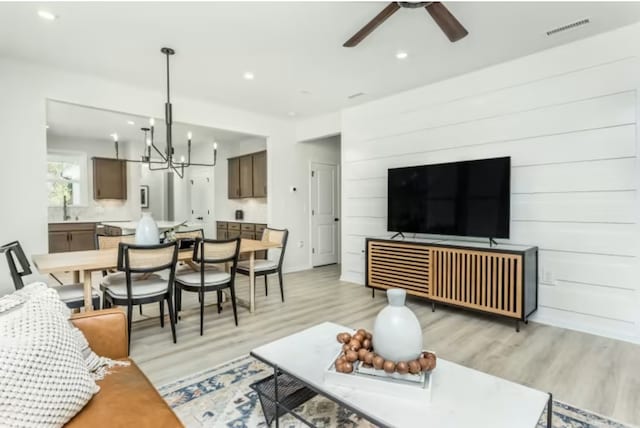 living room featuring ceiling fan with notable chandelier and light hardwood / wood-style floors