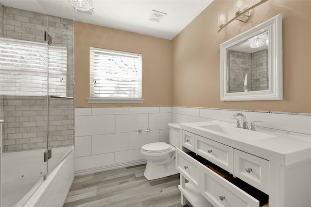 full bathroom featuring vanity, hardwood / wood-style flooring, tile walls, toilet, and tiled shower / bath