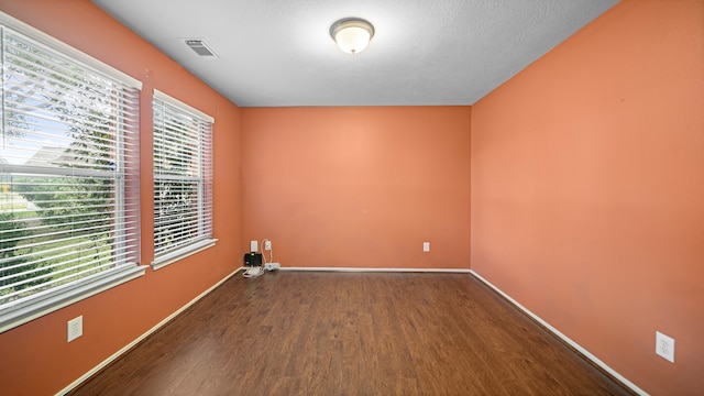 empty room with a textured ceiling, dark hardwood / wood-style floors, and a wealth of natural light