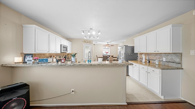 kitchen featuring light stone countertops, white cabinetry, kitchen peninsula, light hardwood / wood-style floors, and appliances with stainless steel finishes