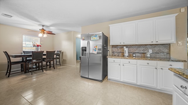 kitchen featuring stainless steel refrigerator with ice dispenser, backsplash, ceiling fan, dark stone countertops, and white cabinets