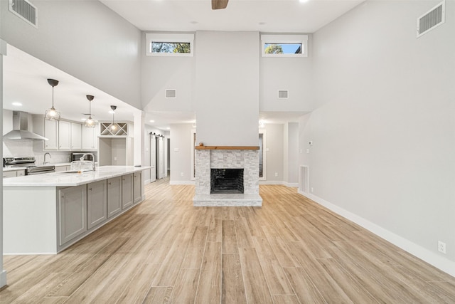 unfurnished living room featuring ceiling fan, sink, a stone fireplace, light hardwood / wood-style flooring, and a towering ceiling