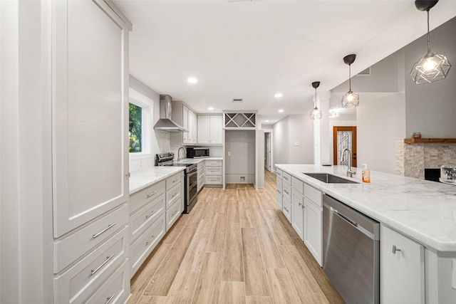 kitchen with appliances with stainless steel finishes, wall chimney exhaust hood, sink, decorative light fixtures, and a stone fireplace