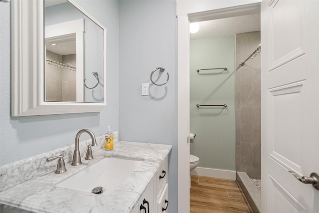 bathroom with toilet, a tile shower, and vanity