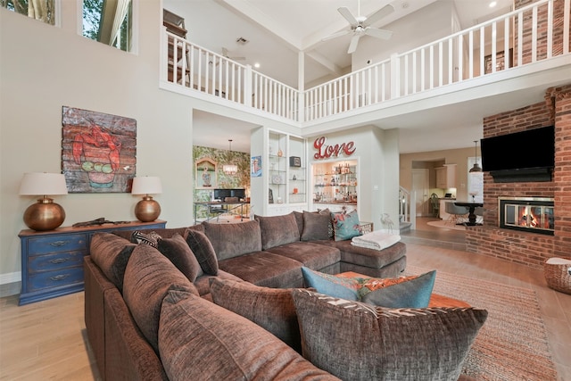 living room featuring ceiling fan, beam ceiling, light hardwood / wood-style flooring, a fireplace, and a high ceiling