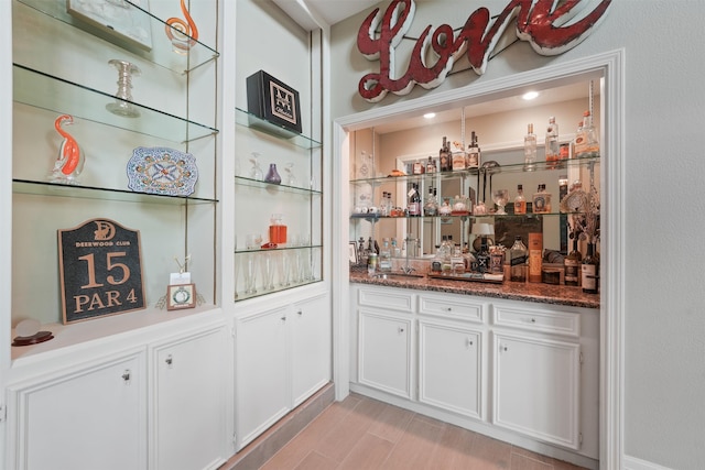 bar featuring white cabinetry, sink, dark stone counters, and light hardwood / wood-style floors