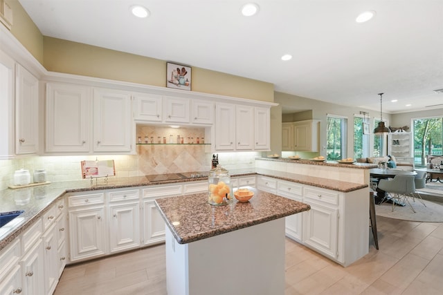 kitchen with light stone countertops, white cabinetry, a kitchen island, and hanging light fixtures