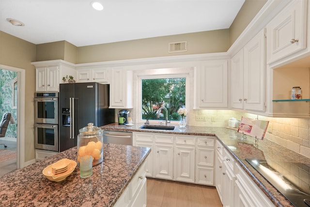 kitchen featuring decorative backsplash, stainless steel appliances, sink, dark stone countertops, and white cabinets