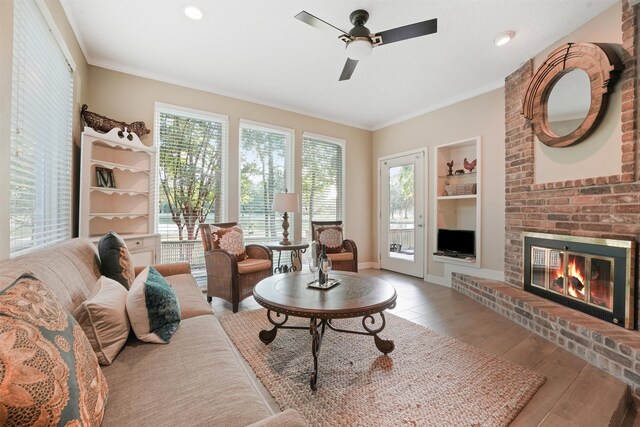 living room featuring a brick fireplace, light hardwood / wood-style flooring, ceiling fan, and ornamental molding