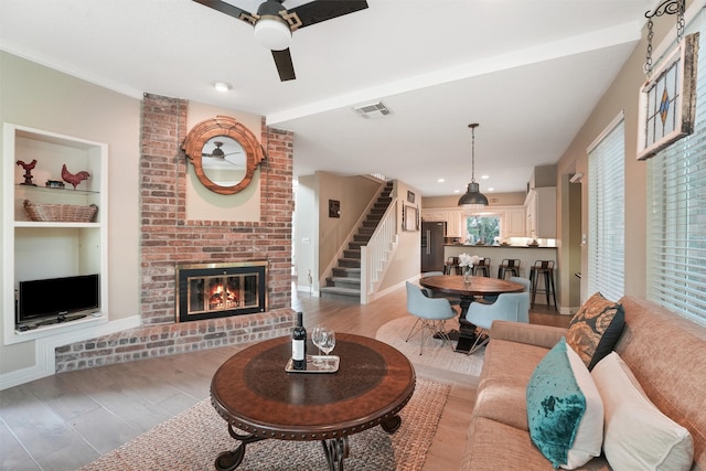 living room with ceiling fan, a fireplace, built in features, and light wood-type flooring