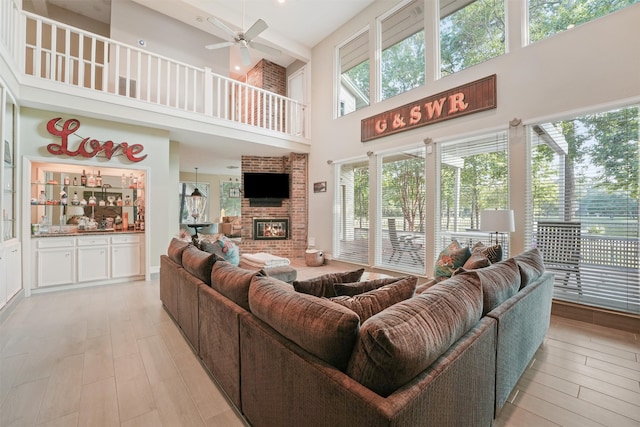 living room with a fireplace, light wood-type flooring, a towering ceiling, and a wealth of natural light