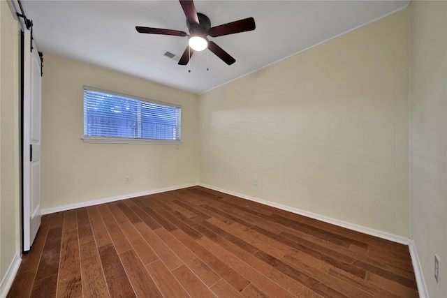 unfurnished room featuring a barn door, dark hardwood / wood-style floors, and ceiling fan