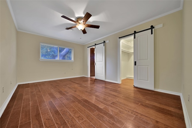 unfurnished bedroom with a barn door, ceiling fan, a spacious closet, and dark hardwood / wood-style floors