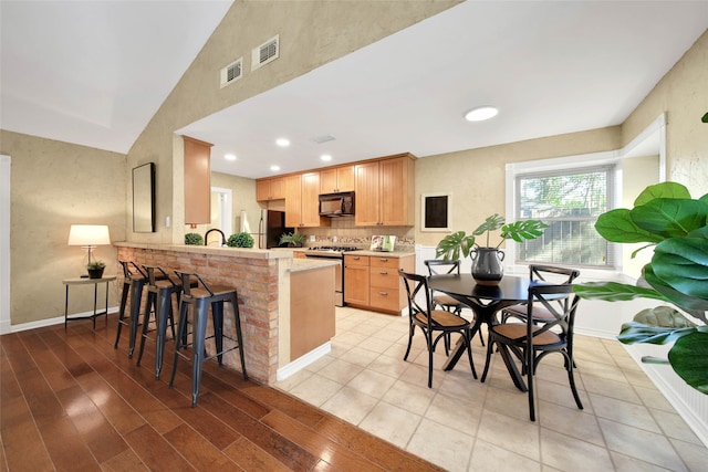 kitchen with kitchen peninsula, appliances with stainless steel finishes, light wood-type flooring, and a breakfast bar