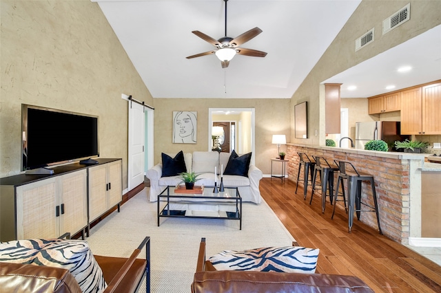 living room featuring ceiling fan, sink, a barn door, high vaulted ceiling, and light hardwood / wood-style floors