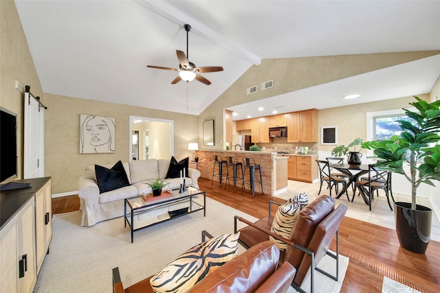 living room with beamed ceiling, ceiling fan, a barn door, and light wood-type flooring