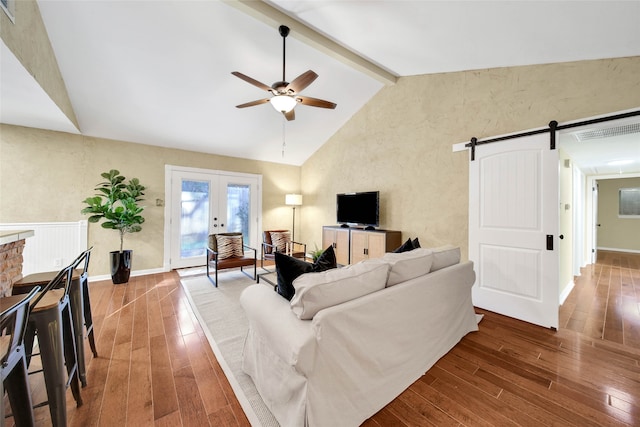 living room with ceiling fan, french doors, a barn door, lofted ceiling with beams, and hardwood / wood-style flooring