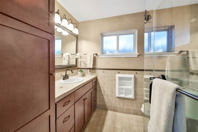 bathroom with tile patterned floors, toilet, a shower with door, vanity, and tile walls