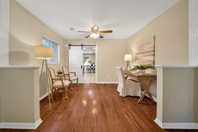 home office featuring hardwood / wood-style floors, ceiling fan, and a barn door