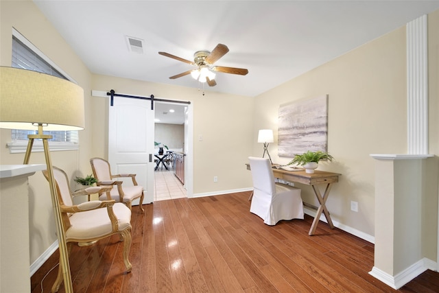 office space with a barn door, ceiling fan, and wood-type flooring