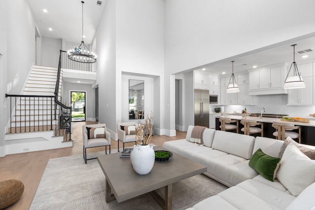 living room featuring visible vents, stairway, a chandelier, light wood-type flooring, and baseboards