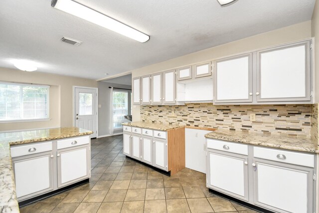 kitchen featuring backsplash, light stone counters, white cabinetry, and light tile patterned flooring