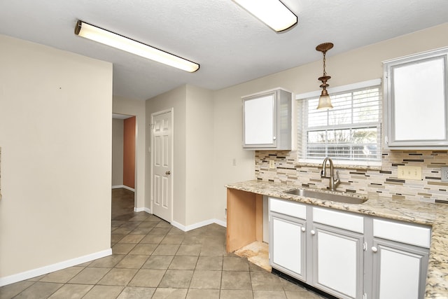 kitchen featuring white cabinetry, sink, tasteful backsplash, light stone counters, and decorative light fixtures