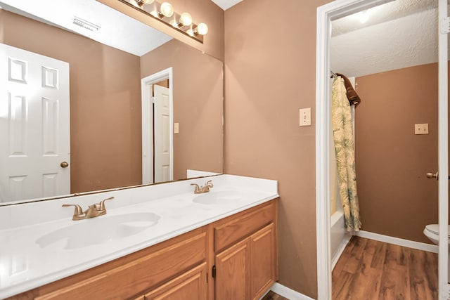 full bathroom featuring hardwood / wood-style floors, a textured ceiling, toilet, shower / tub combo with curtain, and vanity