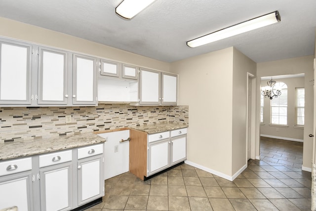 kitchen with backsplash, light stone countertops, white cabinets, and a notable chandelier