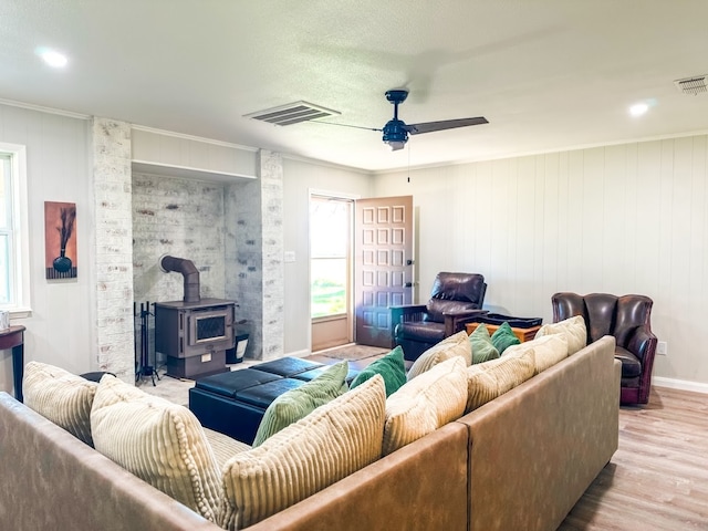 living room featuring wood walls, a wood stove, crown molding, ceiling fan, and light wood-type flooring