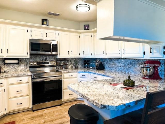 kitchen with light stone countertops, white cabinets, light wood-type flooring, and appliances with stainless steel finishes